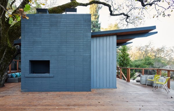 See Arch restored the exterior fireplace wall and painted it a deep blue hue to match the repainted blue timber cladding.