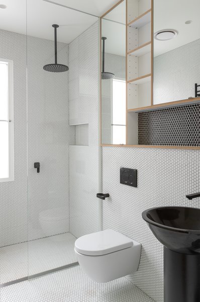 A seamless glass shower screen and matte black fixtures are contemporary additions to this sleek and simple bath. Custom wood cubbies and penny tile on both the walls and floor add a sense of playfulness and texture to the rehabbed bathroom. 