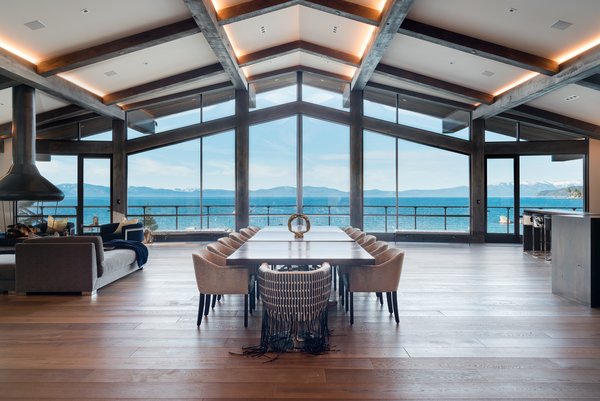 The great room features floor-to-ceiling windows, a floating fireplace, exposed beams, lofty vaulted ceilings, and a multimillion-dollar view. 