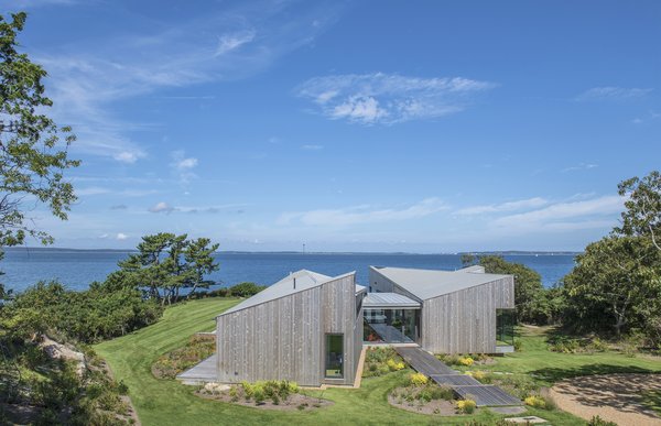 Approached from the driveway, the home is accessed along a stone path that turns into a series of wide, wooden steps. The home's angular roofline is a dramatic form against the natural backdrop, but the wood cladding connects it to the site.