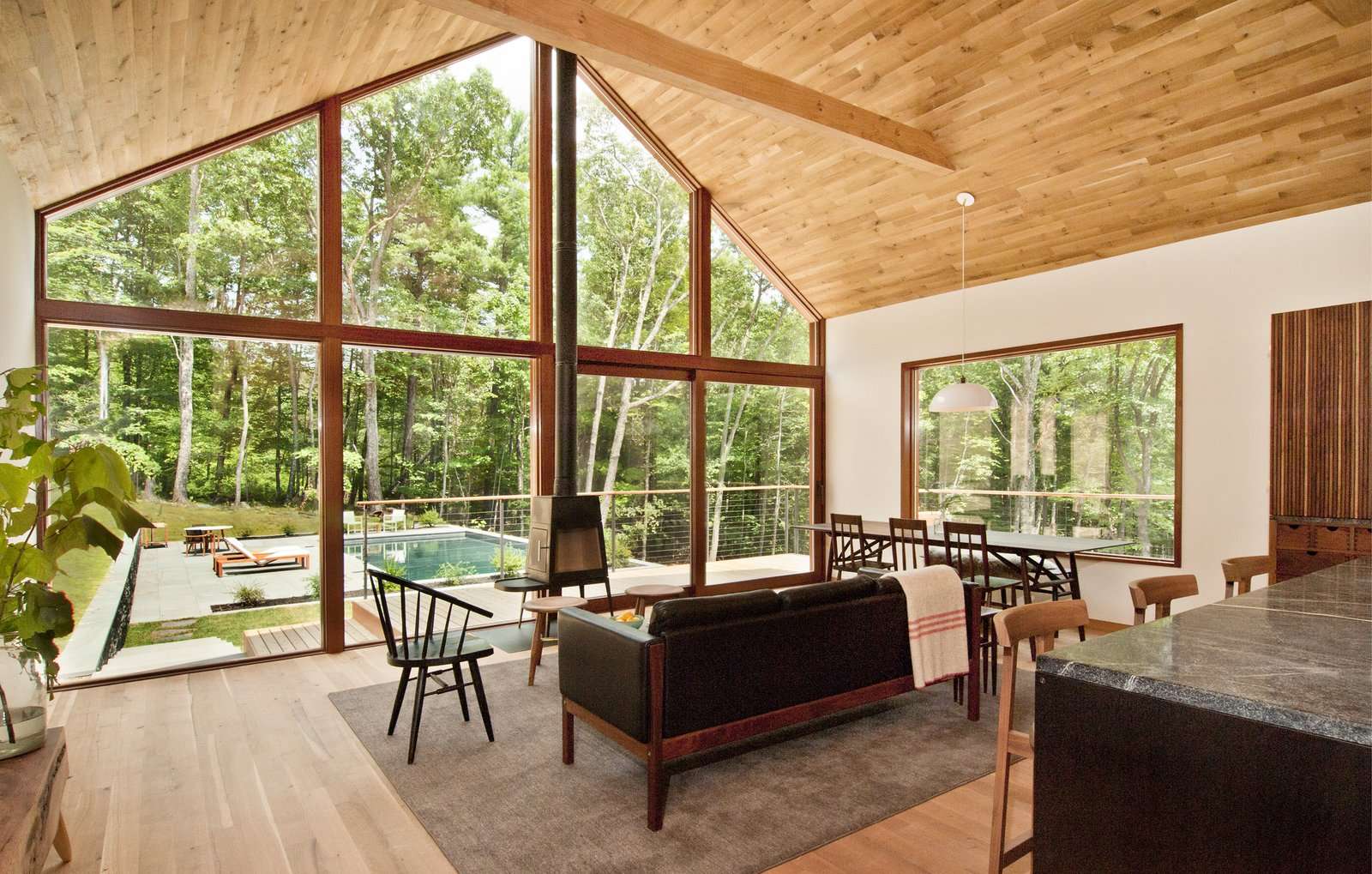 Floor-to-ceiling windows span the entire width of the living room, illuminating the space with natural light. A sliding door provides access to the wraparound porch and pool in the backyard.