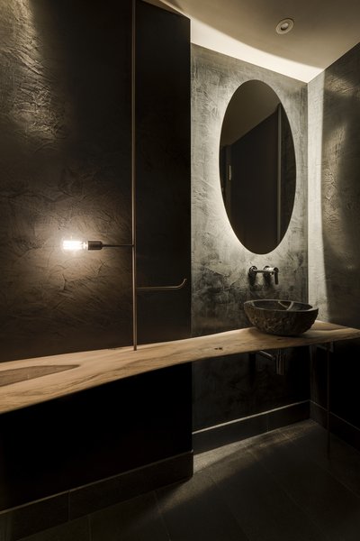 The guest bathroom features an organically shaped wooden table, which is suspended on copper and rests against the textured stucco wall. 