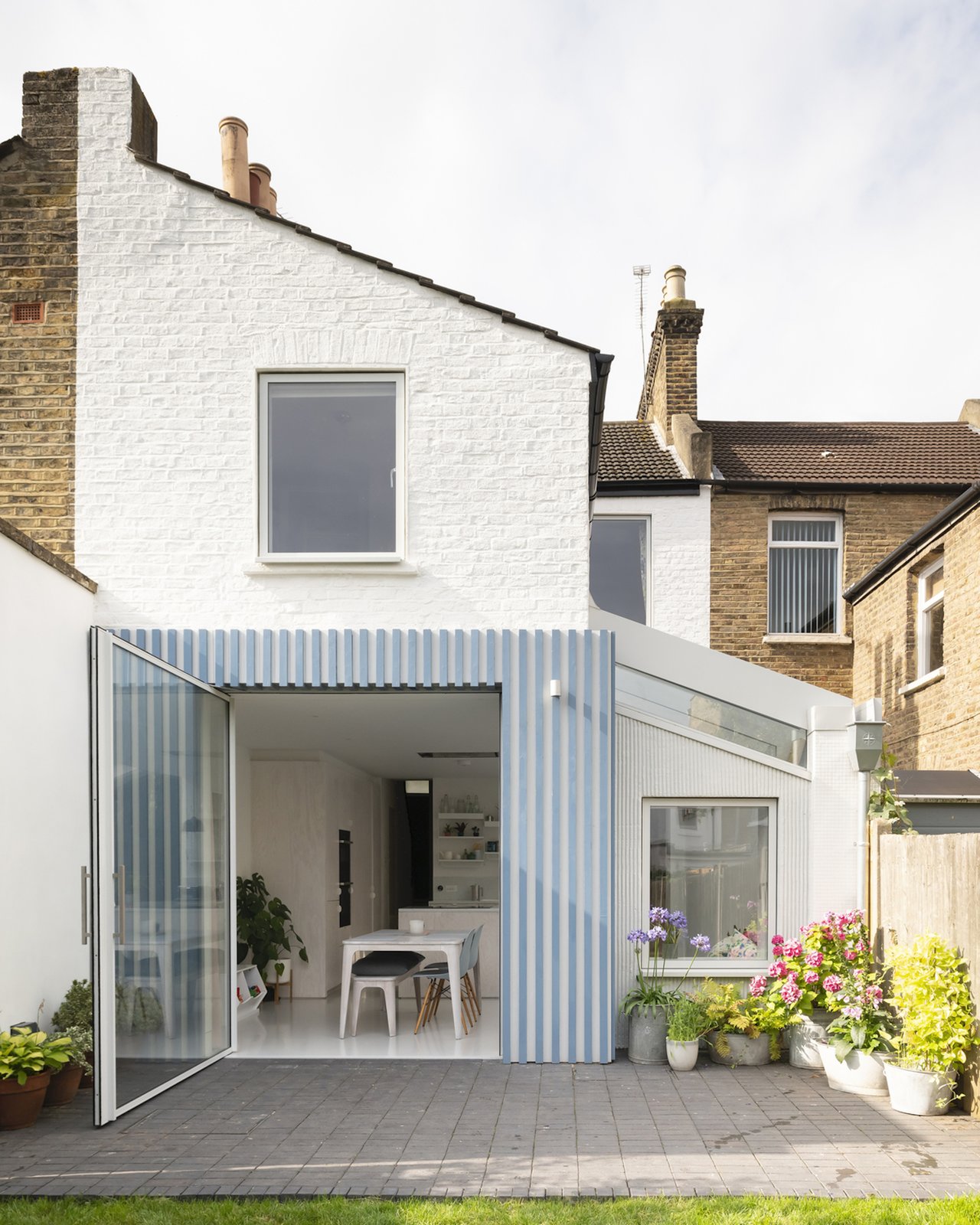 The main volume of the extension is constructed from offset Douglas fir battens painted blue and gray. This reflects the vertical lines and gray color of the ribbed render used in the extension to the side of the house.