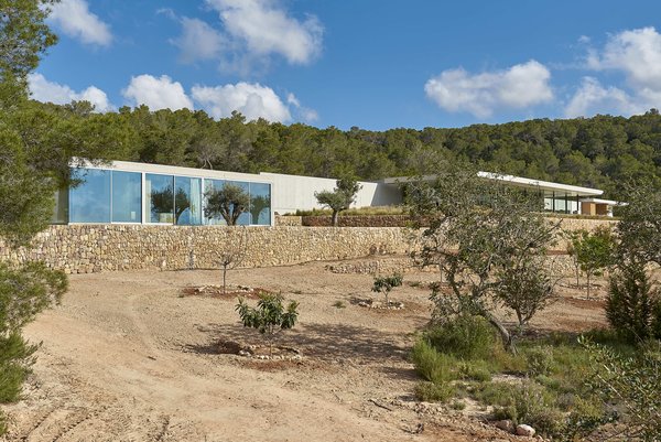 A dirt driveway leads through the natural landscape to the front of the home. The concrete villa is located in Ibiza, one of several islands in an archipelago off the eastern coast of Spain.