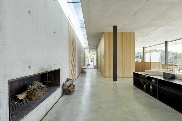 The main entry opens up to an expansive living room, while a long hallway continues behind the kitchen and leads back outside. A skylight appears to divide the home in half, creating an interplay of light, space, and form.