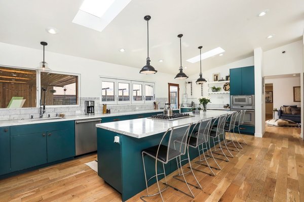 Complete with blue cabinetry, the newly remodeled kitchen features stainless-steel appliances, a marble-topped island, and a line of windows overlooking the covered patio and pool.