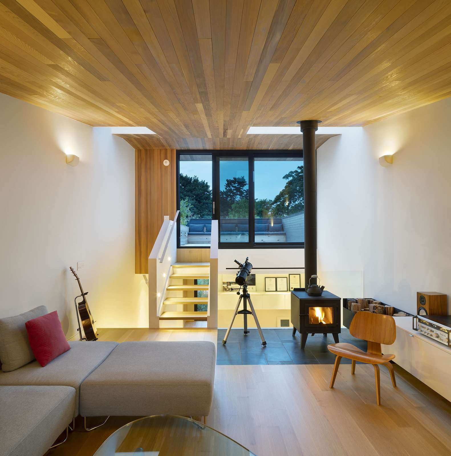 The third floor living room - an urbanized version of a cabin in the woods, with wood stove and cedar ceiling. It nestles intimately into tree tops at one end, and opens widely toward the sky at the other.