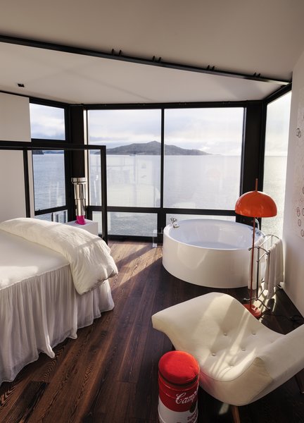 In the master bedroom of a pinwheel-shaped house in Sausalito, California, a circular bathtub sits next to a full-height window with a view of Angel Island. It’s joined by a Vico Magistretti & Mario Tedeschi floor lamp from the 1960s. A lipstick sculpture by Kelly Reemtsen anchors the view north toward Tiburon. The homeowners encouraged architect Mark English to leave the seismic steel frame exposed, to give the white interiors a slightly industrial look.