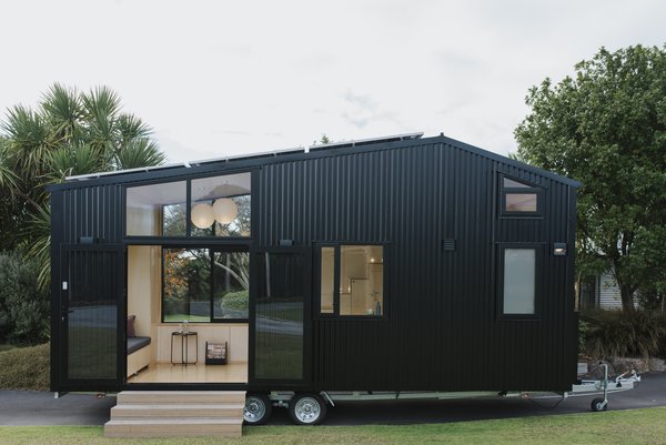 First Light tiny home is sided with black corrugated steel and features expansive windows and French doors that connect the plywood interior to the outdoors.