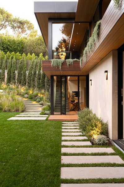 Paved stairs lead down to a lush lawn and the home’s main entrance: a pivoting front door that opens to a two-story atrium. Greenery dangles from planters integrated into the second floor, while additional pavers connect two sliding glass doors in the living room.
