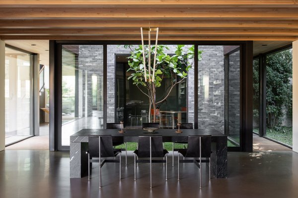 Around the corner from the main entrance, a 23-year-old fiddle leaf fig tree is encased by a glass atrium that pierces the center of the home. The open space directs natural light into both levels of the home—including the dining and living rooms seen here.