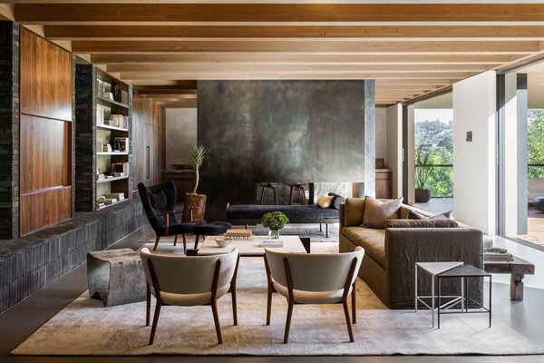 A handsome living room opens to the lawn via disappearing sliding glass doors, while a two-sided fireplace separates the space from the kitchen. The large seating area is bordered by built-in bookshelves and exposed wooden beams.