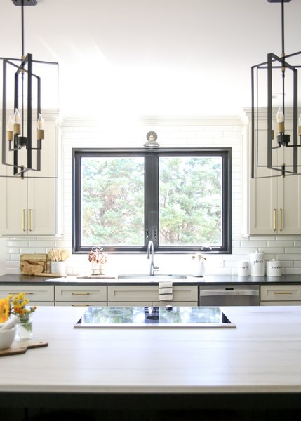 A large picture window over the sink lets in natural light that reflects off the light-colored island countertop. Both the kitchen sink and faucet are from Hausera.