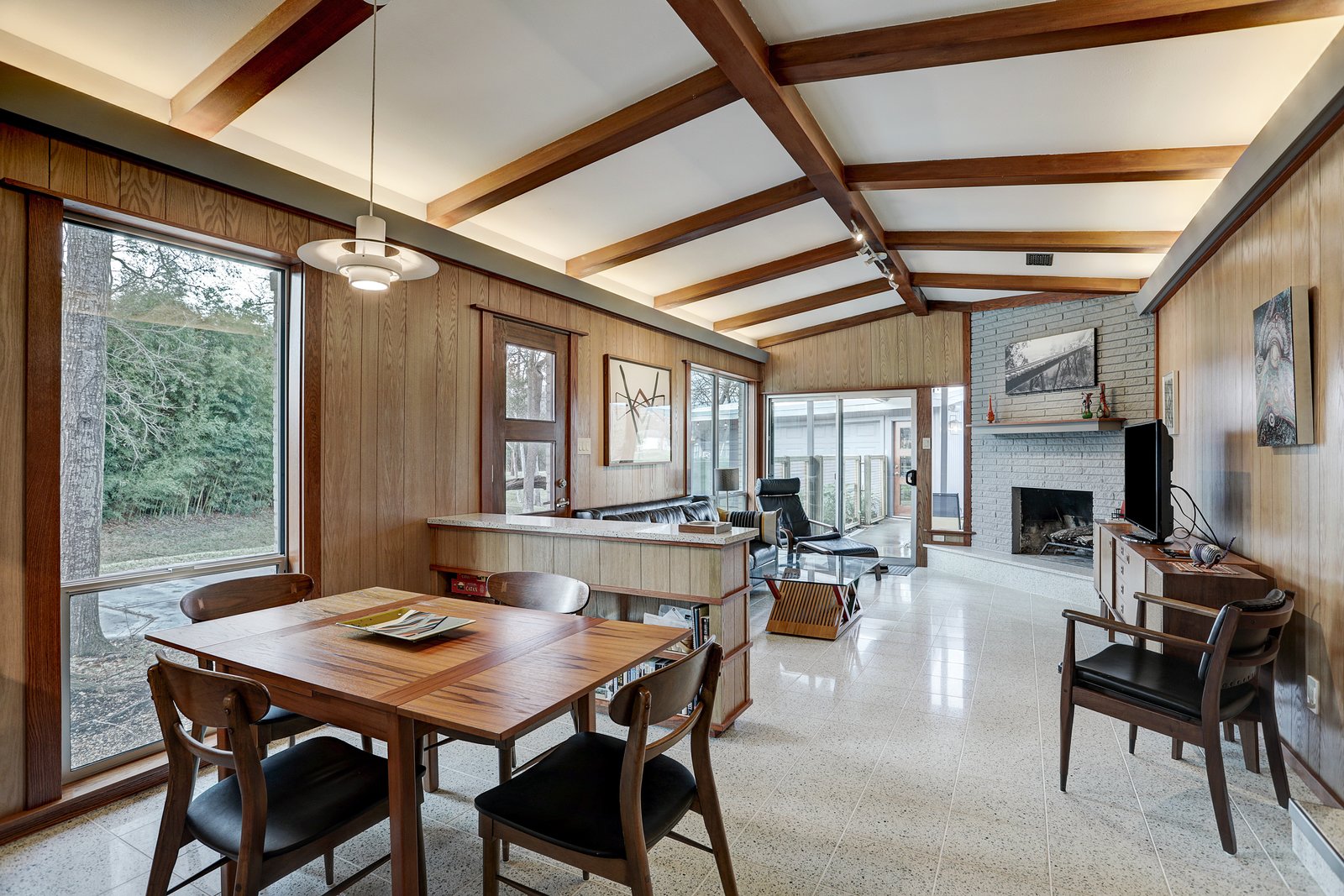 Sporting restored midcentury furniture, the main great room is a time capsule in itself. Wood beams contrast with the crisp white, vaulted ceilings, which provide indirect cove lighting. An original fireplace sits tucked in the corner.