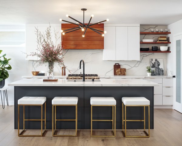 By removing walls and a counter peninsula jutting into the room, interior designer Corine Maggio was able to create enough space for a generous island. The stove wall is a fitting focal point with a hood vent accented in tigerwood and a quartz slab backsplash that helps to tie the space together. 
