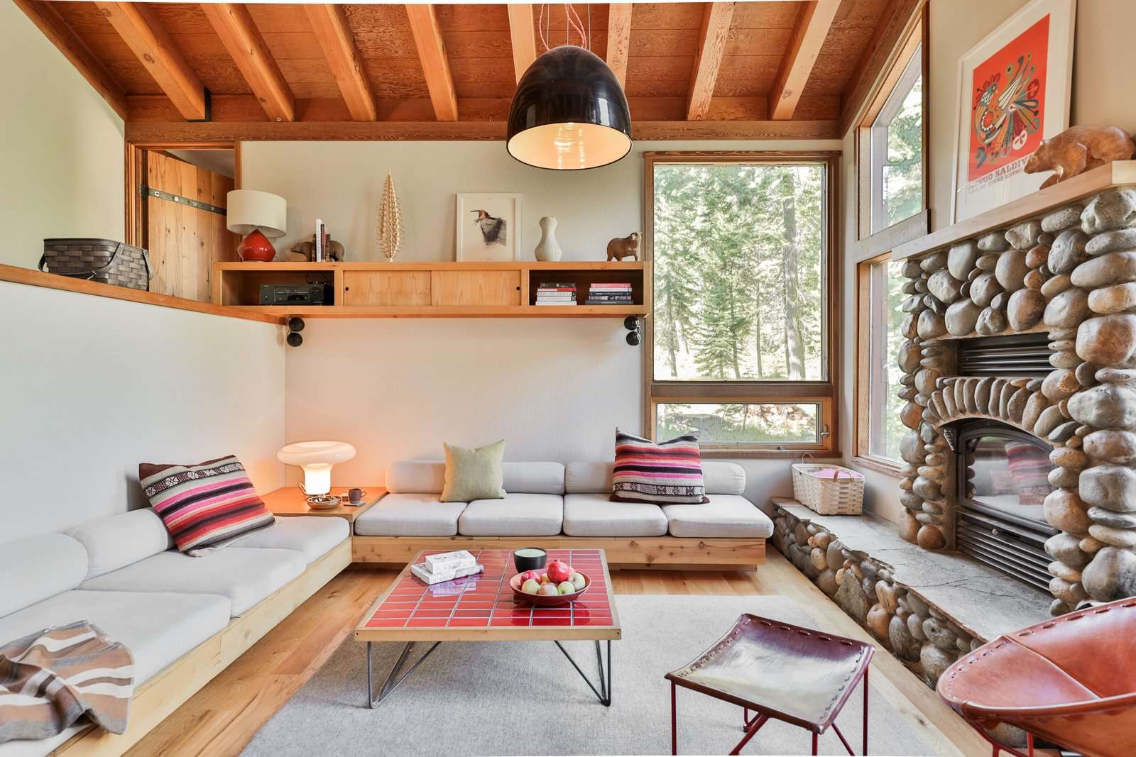 The built-in sofa anchors the living room and faces the existing fireplace. The Leather Oval Chair with a red steel base sits off to the side, and the coffee table was fashioned by attaching vintage steel legs to another tile sample board. 