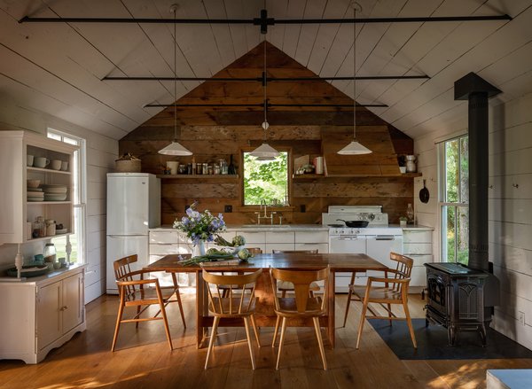 The home’s walls are clad in Oregon white oak reclaimed from a dismantled barn on the property. Jessica chose to paint them white to create a bright, airy look, but she left the kitchen wall au naturel for a visual pop. With storage at a premium, the kitchen needed ample cabinetry as well as some ingenious solutions—including a pull-out cabinet hidden in one half of the range hood. A vintage cabinet on the left wall provides open storage for everyday dishes.