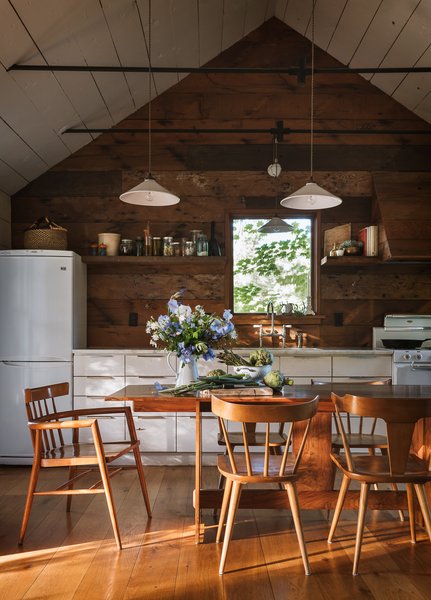 Vintage Paul McCobb chairs set around a handcrafted kitchen table—made by Jessica’s husband from reclaimed Oregon western walnut—delineate the living room from the kitchen/dining space. Pendant lights from a now-defunct French lighting manufacturer illuminate the space, dangling between collar ties that hold the cabin’s roof in place.