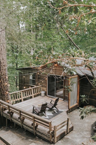 The Cobb Haus, a wood-sided, 700-square-foot cabin in Cobb, California, features a large wood deck surrounded by towering trees.