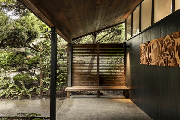 A built-in bench sits outside the entry. The tongue-and-groove siding is painted a rich charcoal.