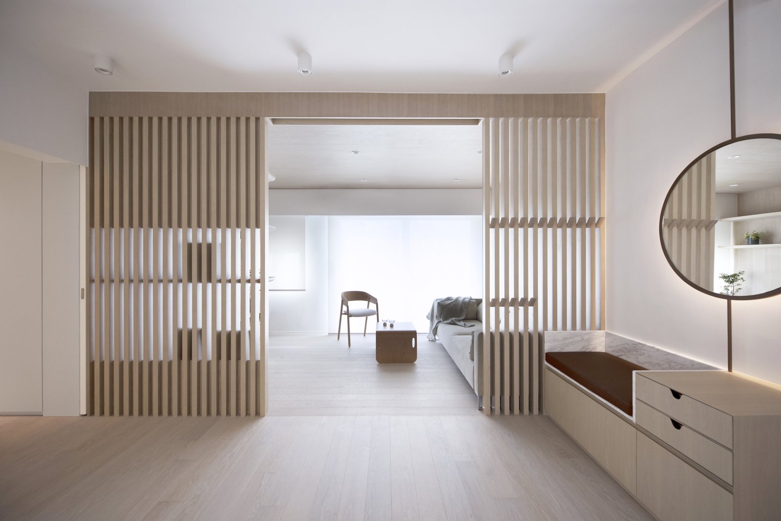 The slatted dividing wall creates a distinction between the living room and the entryway, which is essentially part of a larger open space that includes the dining area.