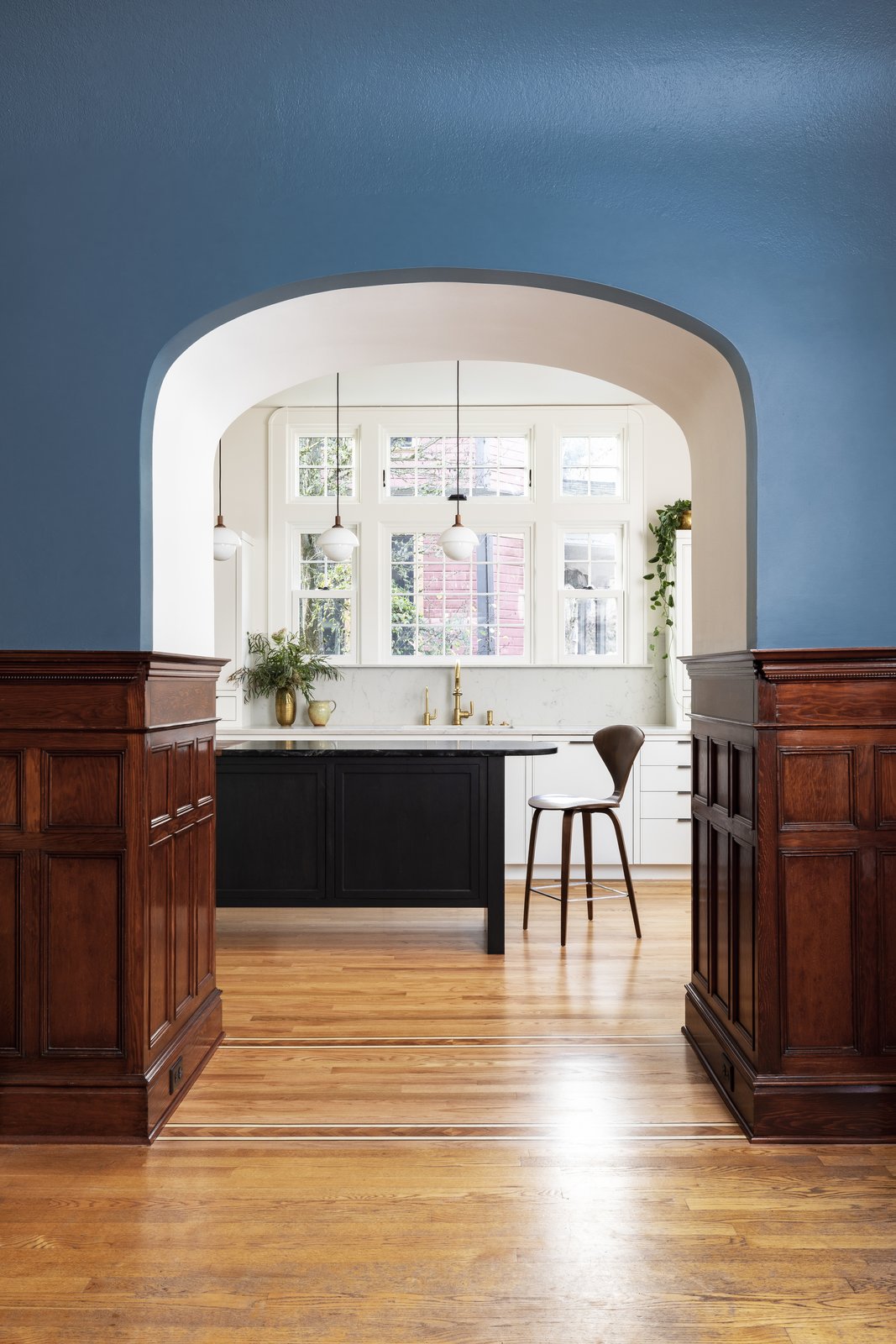 Dyer allocated the entry to the niche, saving and reinstalling the woodwork. It frames a beckoning view of the kitchen, as well as the striking new windows over the sink.