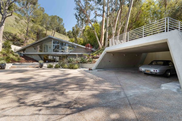 The home’s dramatic triangular facade is nestled into the natural surroundings and features an expansive entry with a geometric carport.
