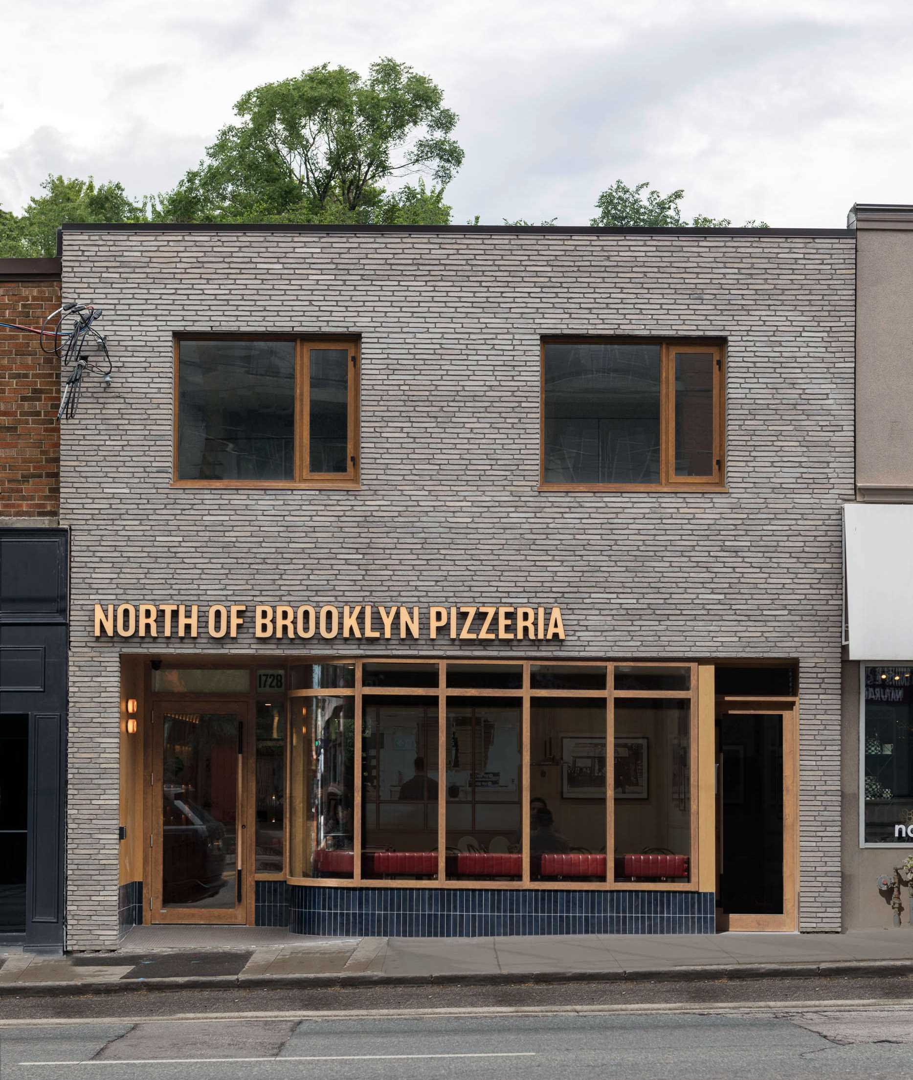 The facade of this pizzeria has been transformed and features light brick, wooden windows, and a curving blue ceramic tile.