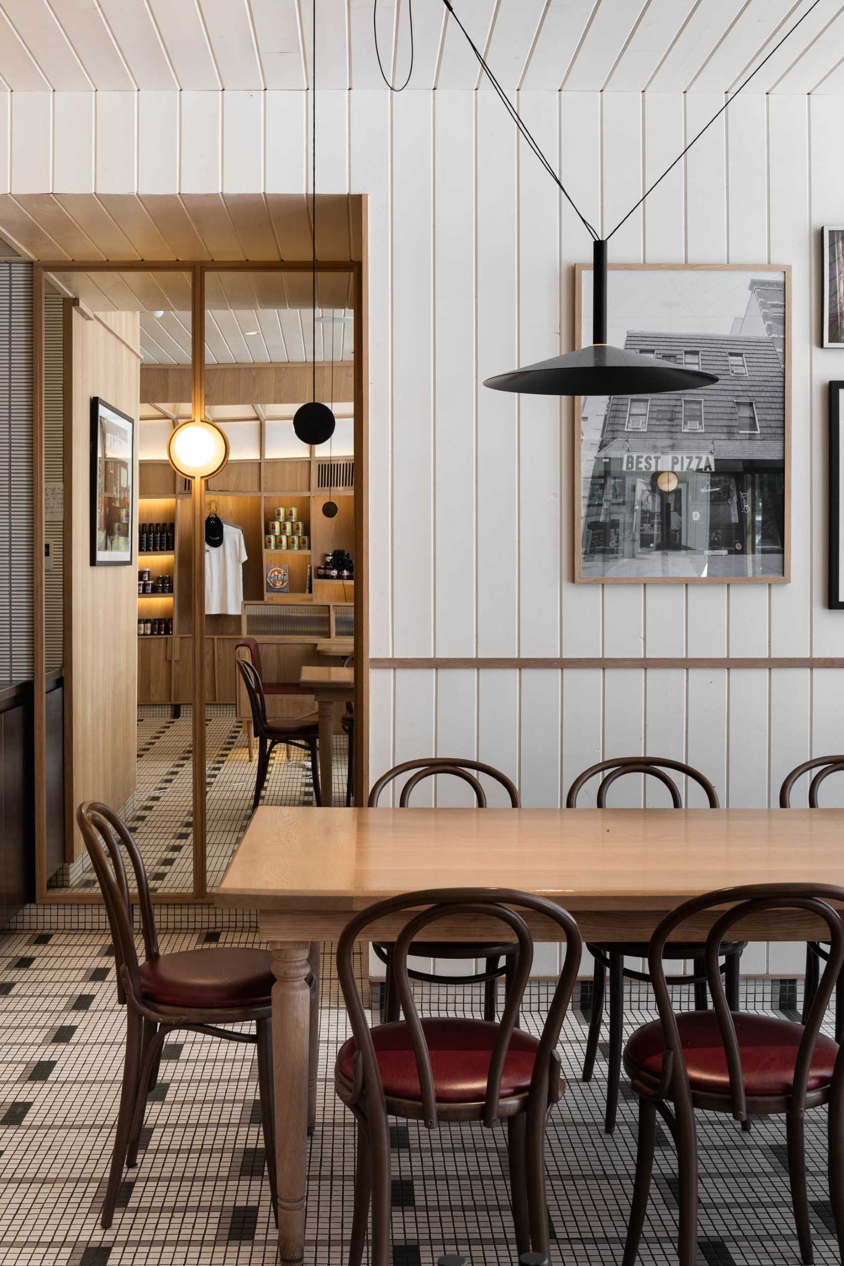 A modern pizzeria that features tile floor, banquette seating, a farm table, and a wall of shelving.