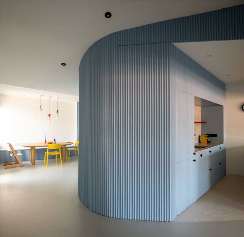 partial interior view of curved fluted blue structure that's part kitchen and divides it with the dining room