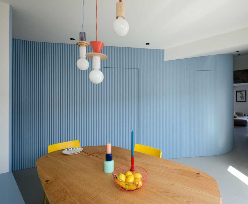 interior view of modern dining room with colorful pendant lights, wood table, and yellow chairs with blue wall behind