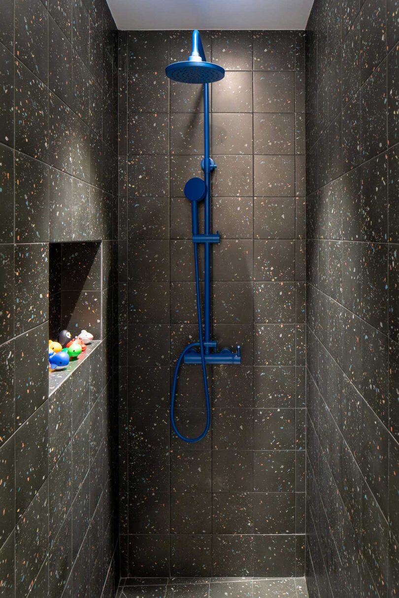 view in dark speckled black tiled shower with bright blue fixtures