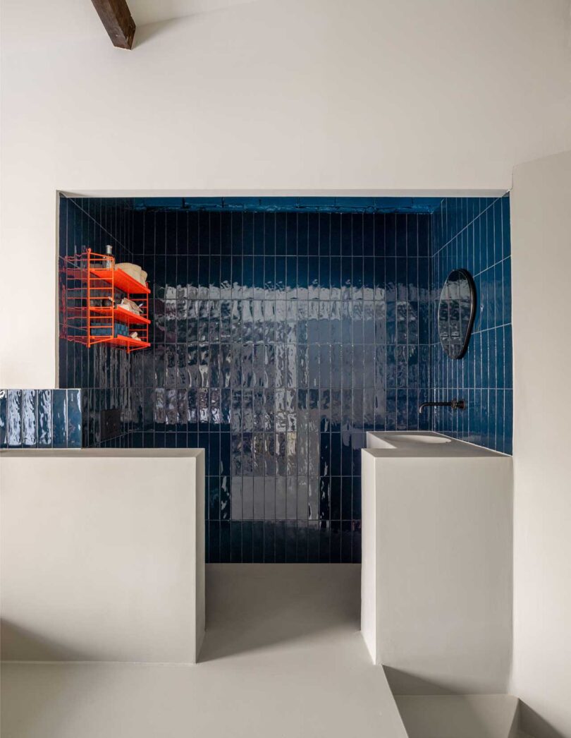 view into open bathroom with dark blue glossy tile and red shelf