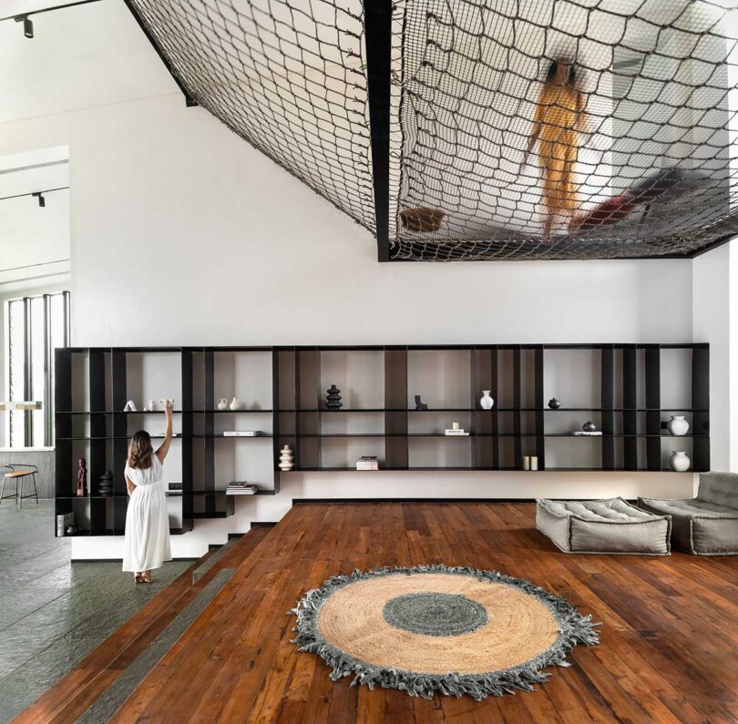 angled view of modern living space with suspended net seating area, wood floors and modern black wall shelves