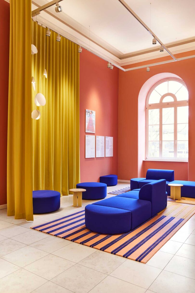angled interior view of modern museum seating area of modular cobalt seating, pink walls, and yellow curtains