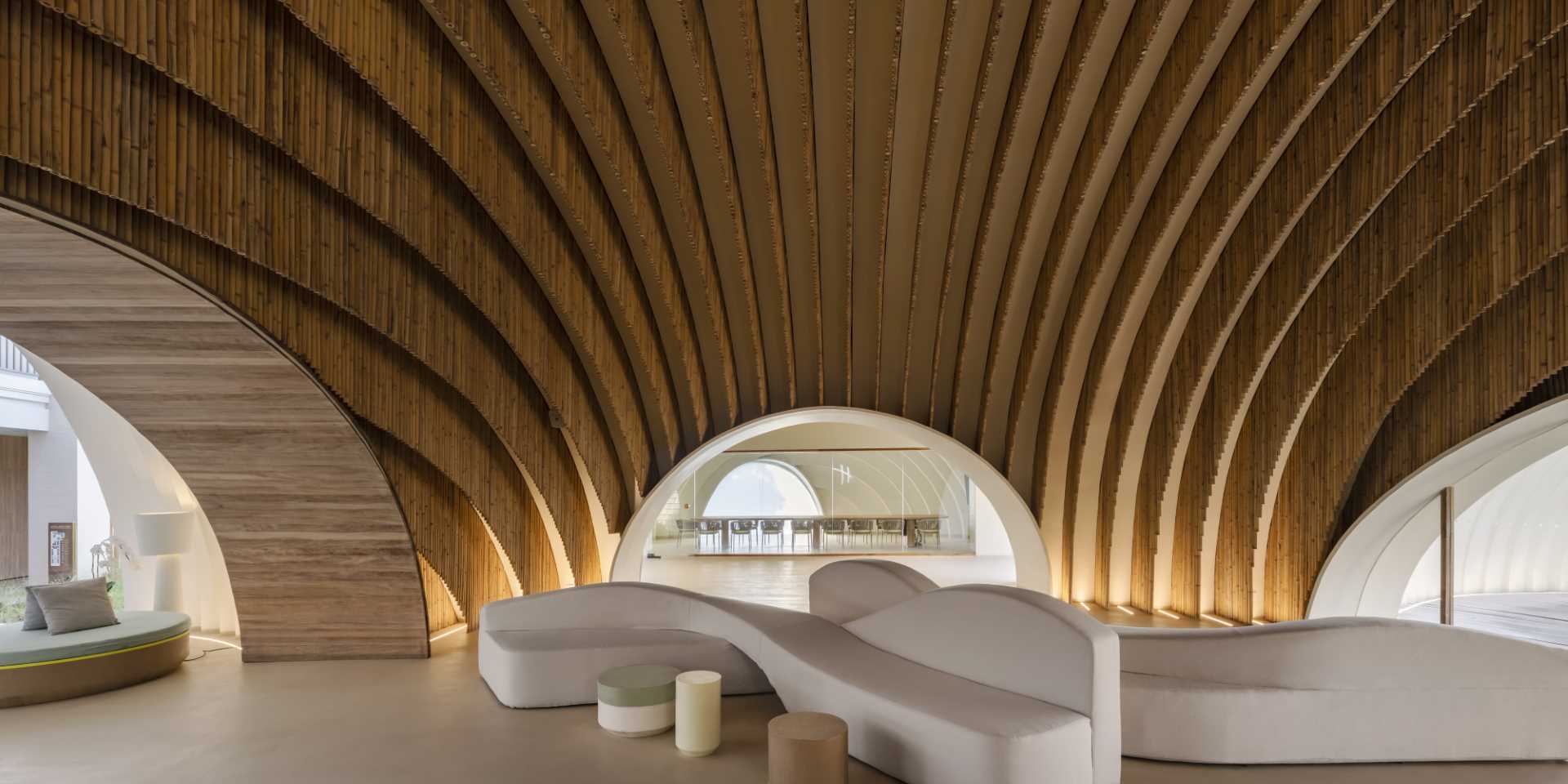 A modern hotel lobby that includes curved walls, hanging planes of bamboo, and hidden lighting that highlights the design.