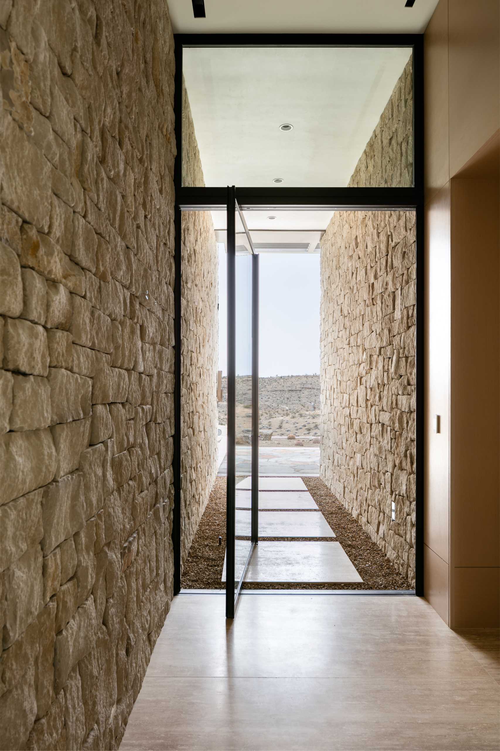 A pivoting glass front door with a black frame welcomes visitors to the home.