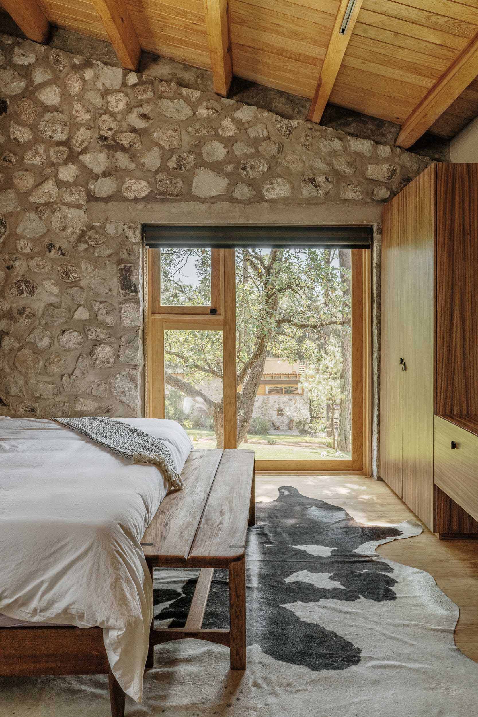 A modern stone and wood bedroom with treetop views.