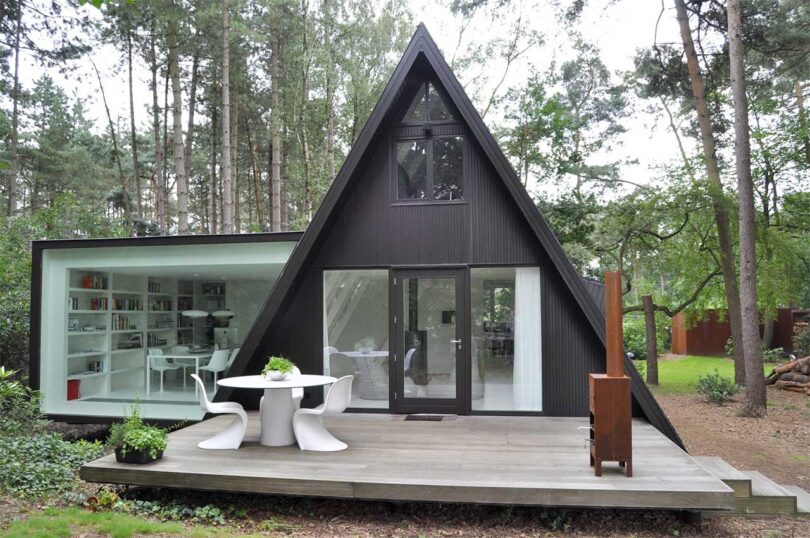 exterior view of modern black a-frame house with side extension and deck with dining table