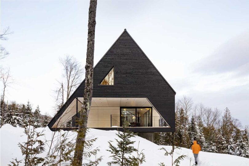 External front shot of a modern black A-frame cabin on a snowy hill