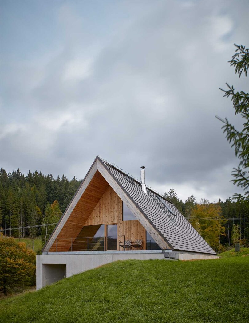 angled exterior view of modern a-frame house behind small grassy hill
