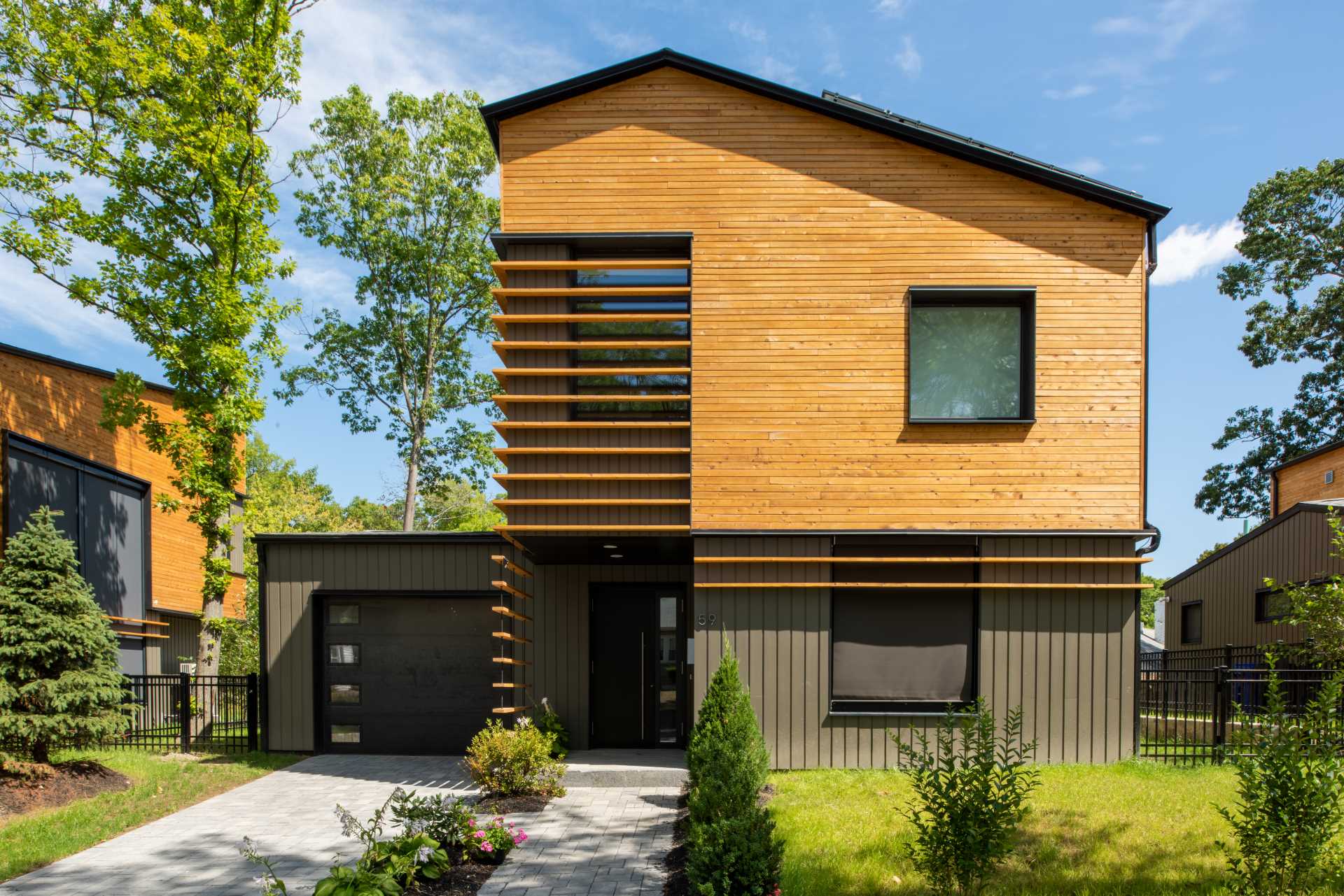 A modern home features an angled roof line, a clear-finished white cedar siding on the upper volume, and a painted siding made from materials recovered from manufacturing by-products on the lower volume.