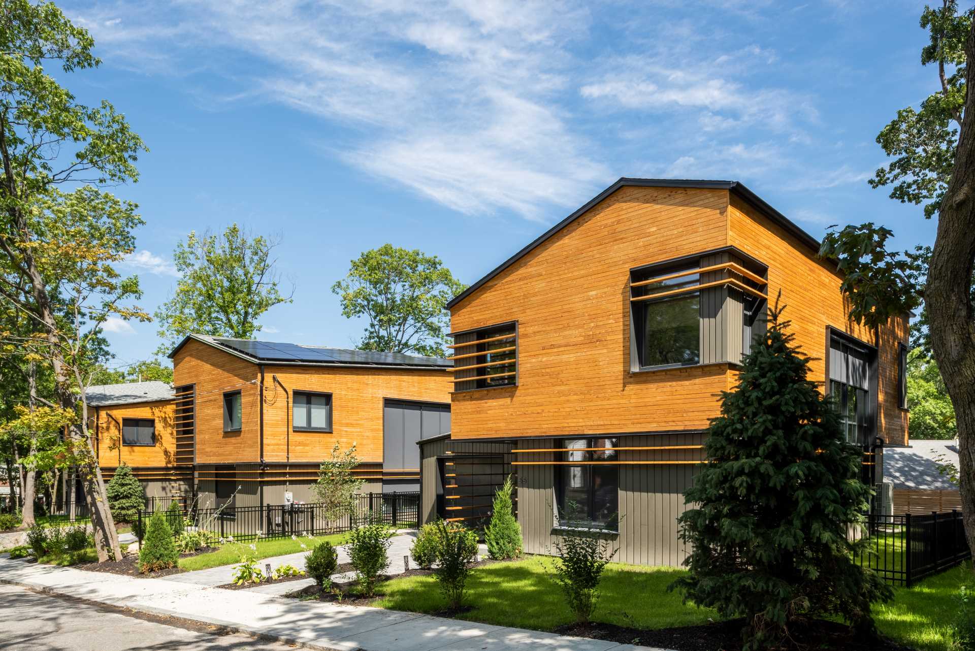 A collection of modern homes feature unique angled roof lines, a clear-finished white cedar siding on the upper volume, and a painted siding made from materials recovered from manufacturing by-products on the lower volume.