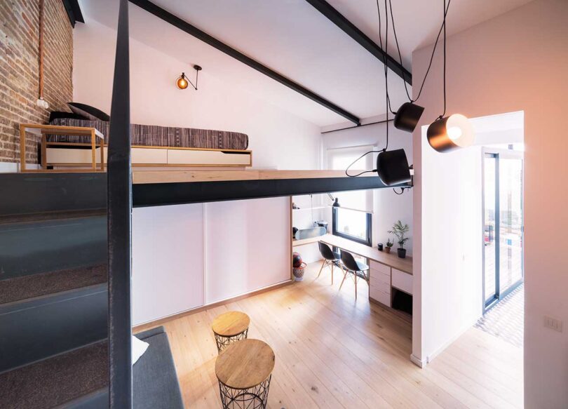 interior view of modern living space with small sectional sofa underneath loft bed with stairs wrapping around