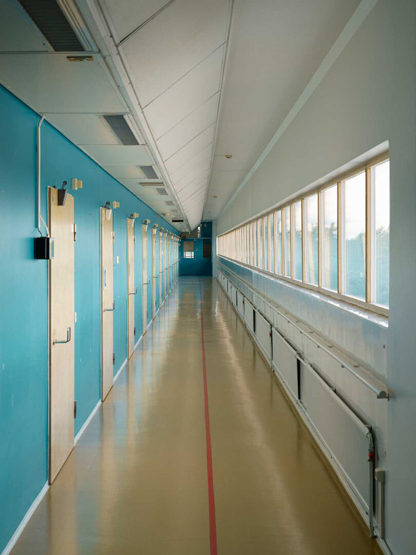 a long hallway with one blue wall full of doors and another of glass