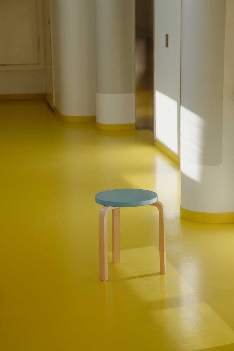 three-legged stool with light blue seat in a space with a yellow floor