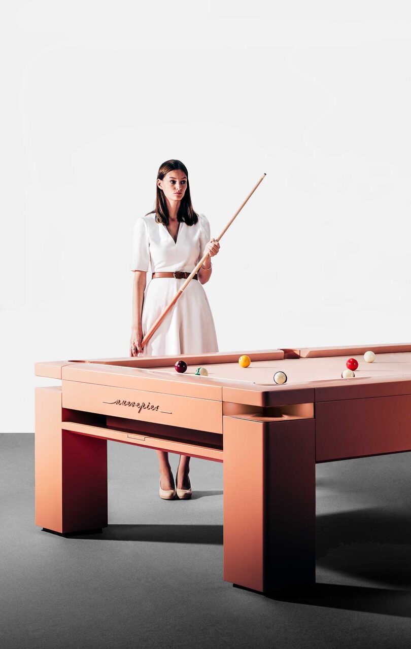 angled set view of woman with pool cue standing behind pale pink modern pool table
