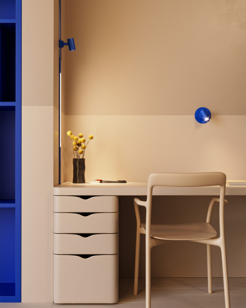 Bold blue vertical MULTIVERSE ribbon installation set along wall near desk and chair with length of ambient lighting module providing additional vertical light and spotlight pointing from above toward small arrangement of flowers in vase on the desk.