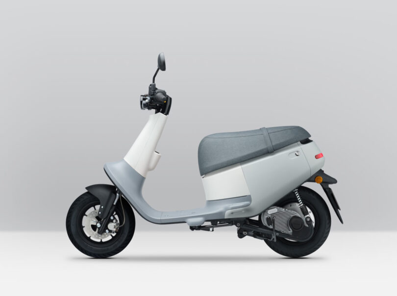 Side profile of Gogoro VIVA ME electric scooter in gray and white colors parked in a light gray painted stage with white flooring.