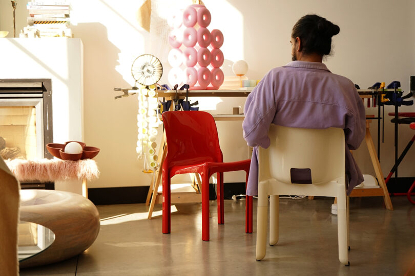 studio space with one red and one white chair and a man sitting in one with his back to the camera